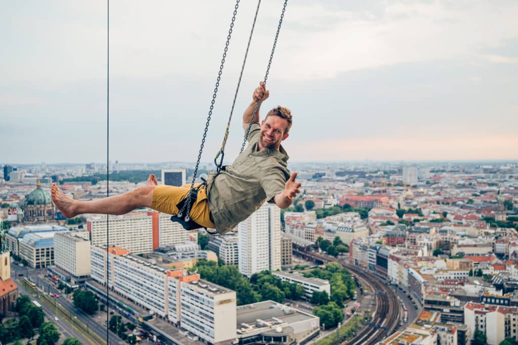 Mann auf einer Schaukel über einer Stadt.